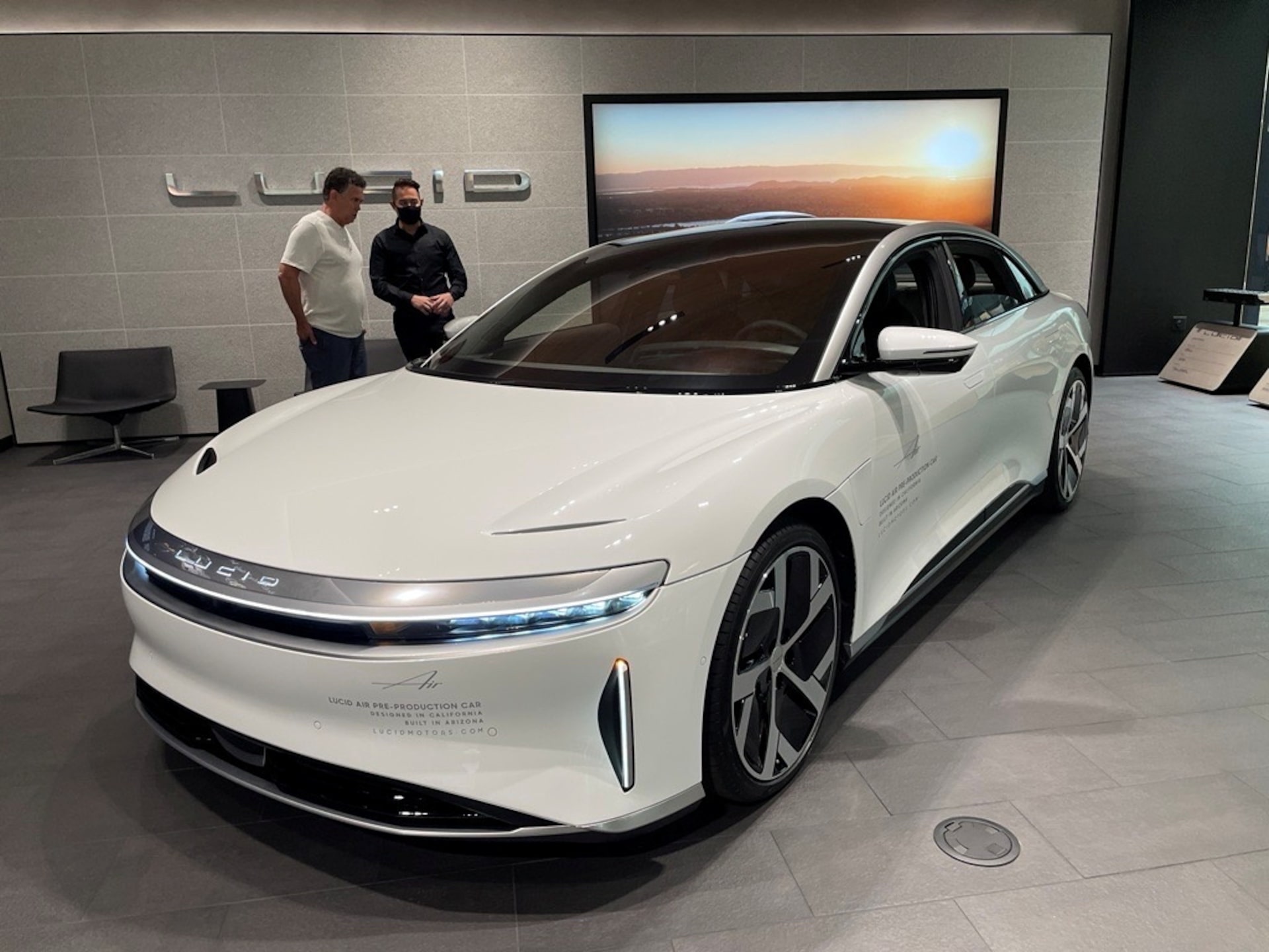 展厅里展示的白色 Lucid Air 电动车，车后站着两名男子，墙上有 LUCID 标志。2021年9月27日美国斯科茨代尔资料照，REUTERS/Hyunjoo Jin；并非此次计划部署的自动驾驶出租车实车。